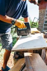 Crop unrecognizable male woodworker cutting wooden plank with electric device while working in countryside.