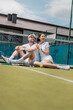 © LIGHTFIELD STUDIOS - cheerful man and woman sitting near tennis net, rackets and ball, summer sport,  leisure and fun