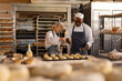 © Wavebreak Media - Focused diverse bakers wearing aprons in bakery kitchen and sprinkling seeds on rolls