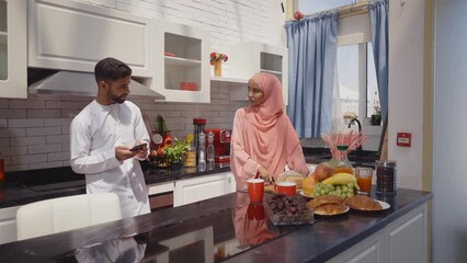 Wall Mural - Happy couple wearing traditional outfits from the emirates spending  time in the kitchen of their beautiful modern apartment in Dubai