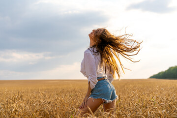 a beautiful young woman stands in a field of wheat with developing hair in the wind against the sky