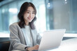 © Surachetsh - Asian office working girl with a radiant smile sits in front of her laptop computer, immersed in work, against a soothing blue turquoise background. generative AI.