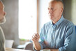 © Mediaphotos - Serious pensive handsome mature man in blue shirt sitting at table and communicating with friend in modern cafe