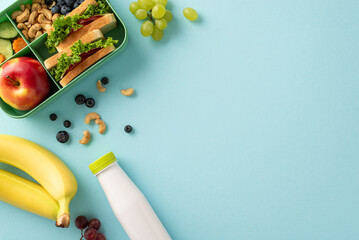 Wholesome lunchtime concept portrayed from a top-down view. The lunchbox holds nutritious sandwiches, fruits, buts and berries on blue isolated background, offering copyspace for text or promotions