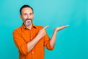 Wall Mural - Photo of confident positive man dressed orange shirt showing finger holding arm empty space isolated turquoise color background
