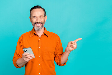 Photo of handsome man with white gray beard wear stylish shirt hold smartphone indicating empty space isolated on teal color background
