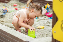 Little Girl Playing In Sandbox At Playground Outdoors. Toddler Playing With Sand Molds.