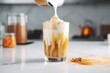 Leinwanddruck Bild - Pouring milk into a glass with warm coffee drink with pumpkin spice or cinnamon, whipped milk foam and chocolate in a white sunlit modern kitchen interior. Generative AI technology