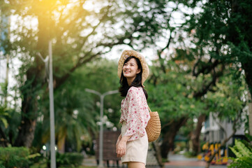 Portrait of asian young woman traveler with weaving hat and basket happy smile on green public park nature background. Journey trip lifestyle, world travel explorer or Asia summer tourism concept.