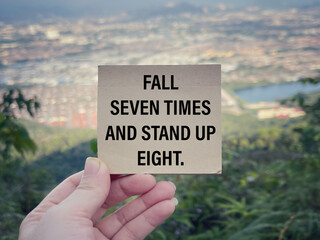 Motivational and inspirational wording. Fall Seven Times And Stand Up Eight written on a small paper. With blurred vintage styled background.