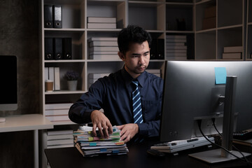 Poster - Tired young Asian businessman working overtime in the office room at night, trying to get things done before the deadline.