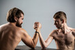 © Yevhen - Arms wrestling thin hand, big strong arm in studio. Two man's hands clasped arm wrestling, strong and weak, unequal match. Arm wrestling. Heavily muscled bearded man arm wrestling a puny weak man