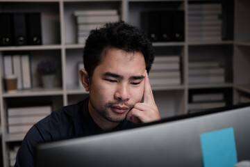 Poster - Tired young Asian businessman working overtime in the office room at night, trying to get things done before the deadline.