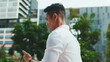 © Andrii Nekrasov - Young businessman is walking down the street and looking at a smartphone on modern building background