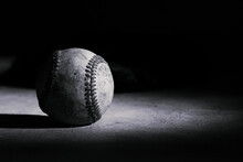 Spotlight On Old Used Baseball Ball In Black And White With Dark Background.