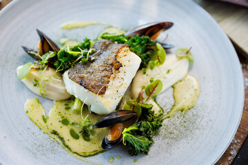 Wall Mural - Cod fillet with cauliflower cream, asparagus, clam-wine sauce and mussles. Delicious seafood fish closeup served on a table for lunch in modern cuisine gourmet restaurant