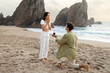 © Prostock-studio - Full length shot of loving man with engagement ring proposing to surprised lady, guy standing on knee on ocean beach
