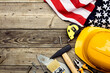 © photoguns - Happy Labor day American national holiday greeting card template. Flat lay yellow safety helmet, flag of USA, building tools on wooden table. Top view.