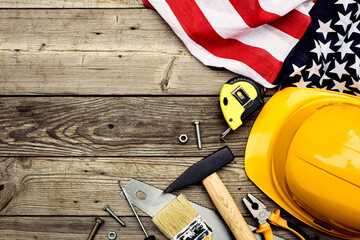 Happy Labor day American national holiday greeting card template. Flat lay yellow safety helmet, flag of USA, building tools on wooden table. Top view.