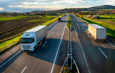 Wall Mural - Highway transport. Transportation Trucks in lines passing on a rural countryside highway under a beautiful blue sky