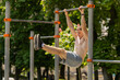 Athletic topless muscular man training abs, doing abdominal crunches, pull-ups exercises on horizontal bar. Young shirtless guy on playground. Sports health fitness routine workout strength gymnastics