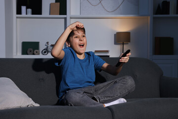 Wall Mural - Emotional boy watching TV and holding remote control on sofa at home