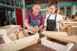 © EKKAPON - Senior male carpenter instructing young woman to use equipment while working at carpentry workshop.