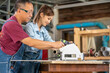 Portrait of senior carpenter teaching apprentice standing at table in workshop