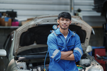 Asian man mechanic in uniform with crossed arms standing at the car repair station.