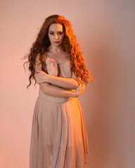 Wall Mural - Close up portrait of beautiful brunette  female model wearing a cream dress with golden back light lighting.
Gestural arm poses with hands reaching out, isolated on studio background.
