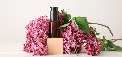 Bottle of essential oil with beautiful lilac flowers on light background