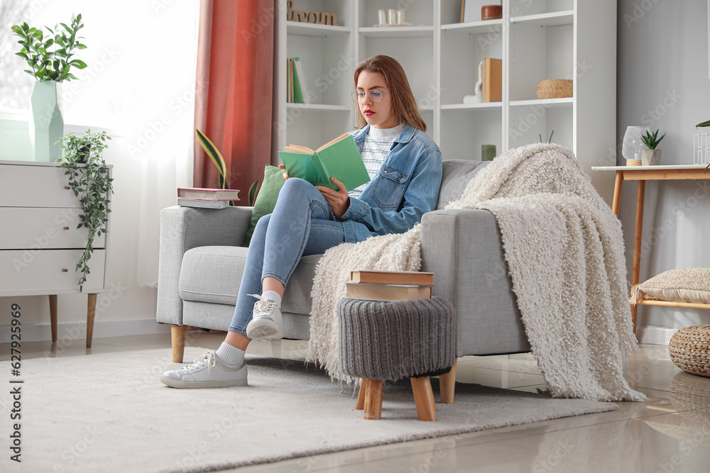 Young woman reading book on sofa at home