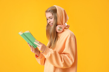 Wall Mural - Young woman reading book on yellow background