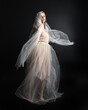 © faestock - Full length portrait of beautiful woman wearing white gown dress with flowing ghostly veiled fabric, isolated on dark studio background.