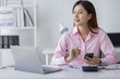 © David - Asian Woman entrepreneur busy with her work in the office. Young Asian woman talking over smartphone or cellphone while working on computer at her desk.