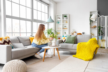 Wall Mural - Beautiful young woman sitting on cozy sofa near big window in living room