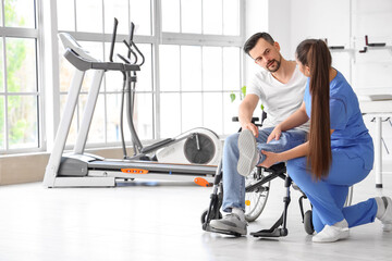 Wall Mural - Female physiotherapist working with young man in wheelchair at rehabilitation center