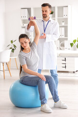 Wall Mural - Male physiotherapist working with young woman in rehabilitation center