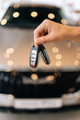 © dikushin - Vertical closeup cropped shot of unrecognizable buyer male holding in hand car key from new auto after buying at showroom on blurred background of new auto. Concept of choosing and buying new car.