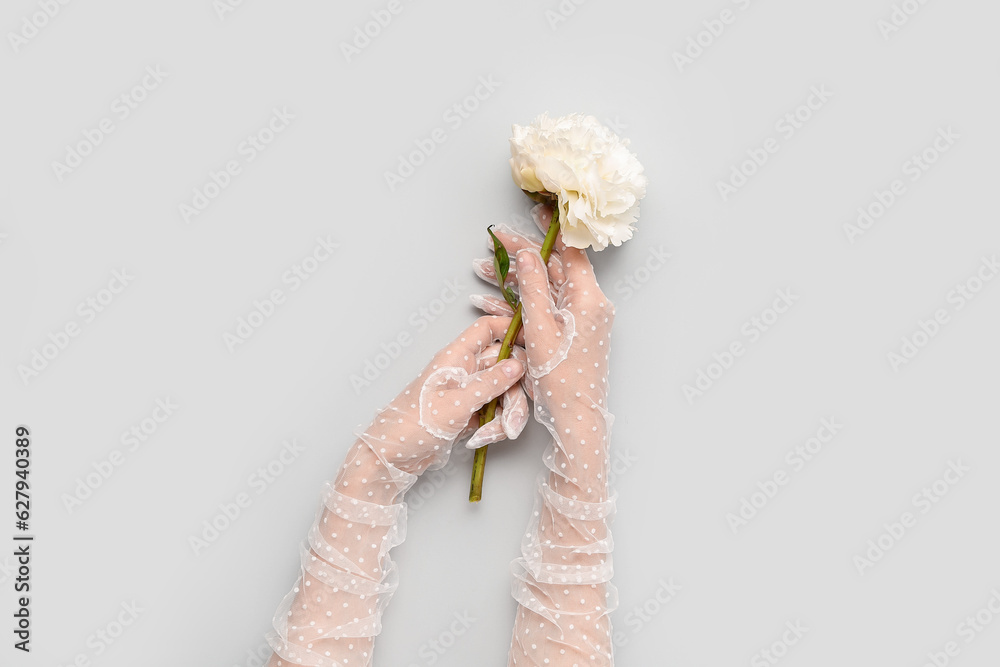 Female hands in laced gloves with beautiful peony flower on light background