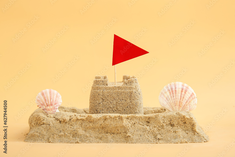 Castle made of sand with seashells and flag on orange background