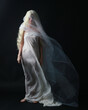 Full length portrait of beautiful blonde woman wearing white gown dress with flowing ghostly veiled fabric, isolated on dar studio background.