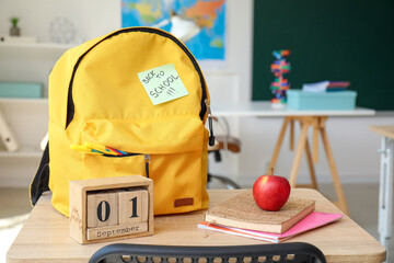 Wall Mural - Backpack, stationery, calendar and sticky note with text BACK TO SCHOOL on desk in classroom