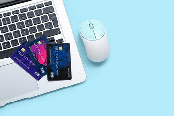 Laptop with computer mouse and credit cards on blue background