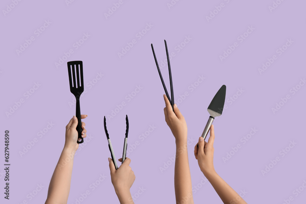Female hands with tongs and spatulas on lilac background