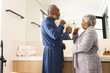 Happy senior biracial couple wearing bathrobes and brushing teeth in bathroom at home