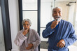 Portrait of happy senior biracial couple wearing bathrobes and brushing teeth in bathroom at home