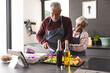 © WavebreakMediaMicro - Happy senior biracial couple wearing aprons preparing vegetables in kitchen at home