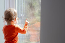 Baby Girl Standing In Front Of The Window And Point Finger Glass At Sunny Day, Having Fun With The Sunbeams, Natural Dirty Home Glass