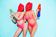 Two Beautiful Sexy Women In Red Underwear. Models Wearing Bandit Balaclava Mask. Hot Seductive Female In Nice Lingerie Posing Near Blue Wall In Studio. Crime And Violence. Hold Water Gun